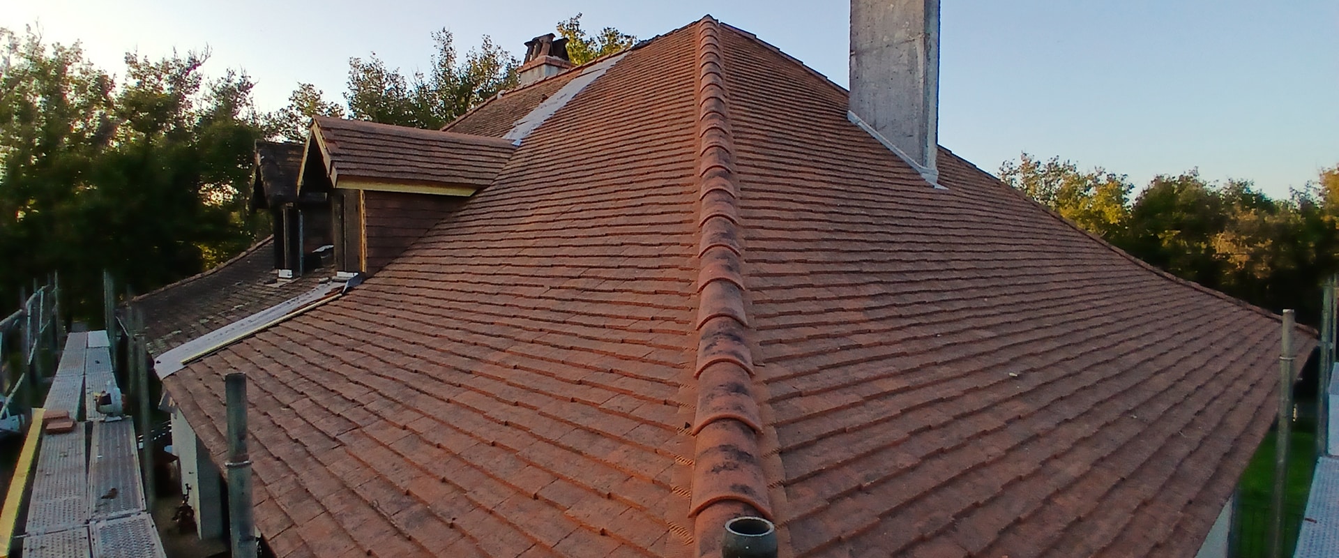 Toiture en tuiles rouges en cours de rénovation avec échafaudage visible, cheminée en béton et faîtage arrondi.